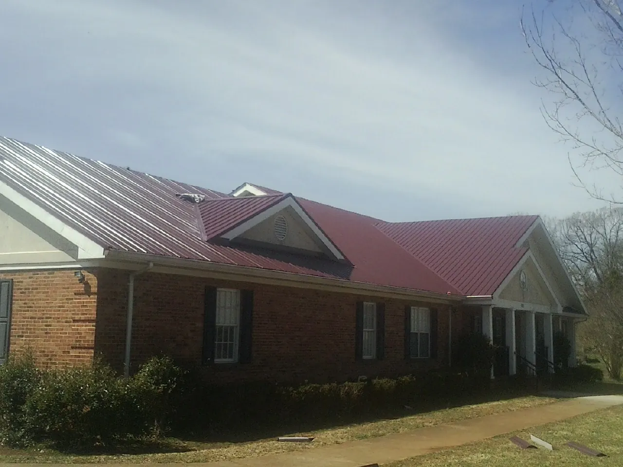 Red metal roof with gabled entries on a long brick building, from a Hail Damage Roof Repair job in Capac