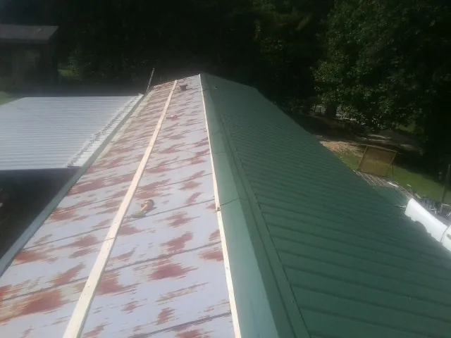 Old rusted panels beside newly installed green metal roofing — Wind Damage Roof Repair by Roofing Brothers in Capac