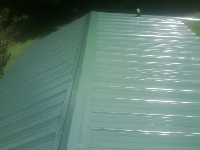 New green metal panels meeting at the ridge of a roof — Flat Roof Repair work by our crew in Capac
