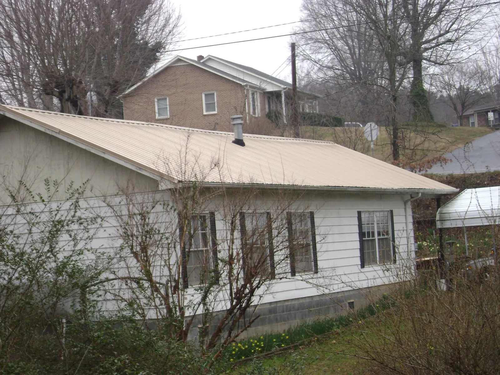 Tan metal roof on a white sided house set into a hillside — Commercial Roofing by Roofing Brothers in Capac